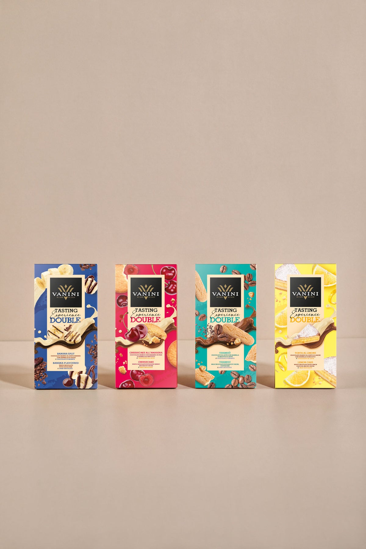Collezione Vanini Double Tasting Experience composta da quattro tavolette di cioccolato gourmet disposte in fila su sfondo beige. Le confezioni dai colori vivaci rappresentano gusti ispirati ai dessert più amati: Banana Split, Cheesecake all’Amarena, Tiramisù e Torta al Limone. Ogni packaging è arricchito da illustrazioni degli ingredienti caratteristici, come banane, amarene, chicchi di caffè e fette di limone, che richiamano il doppio incontro di sapori racchiuso nelle tavolette.