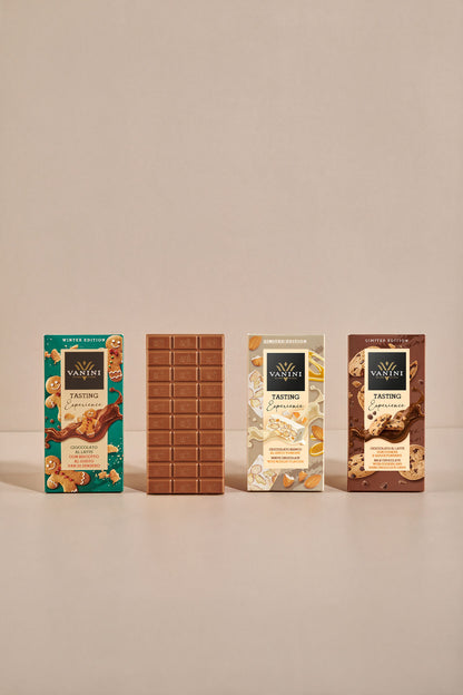 Assortimento Vanini Tasting Experience Winter Edition con quattro referenze di cioccolato ispirate ai dolci delle festività. Al centro della composizione è esposta una tavoletta di cioccolato al latte aperta, che mostra il caratteristico stampo Vanini. Le confezioni celebrano gusti come pan di zenzero, torrone e biscotti con gocce di cioccolato, con grafiche raffinate e ingredienti illustrati su sfondo chiaro e minimalista.