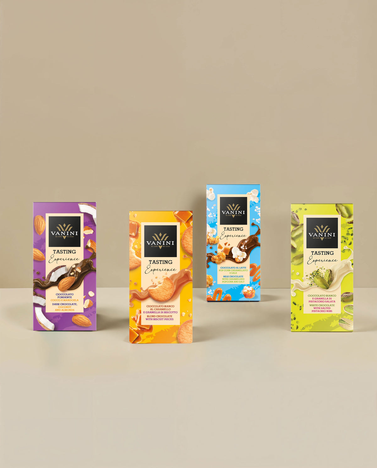 Collezione Vanini Tasting Experience composta da quattro tavolette di cioccolato assortite disposte su sfondo beige minimalista. Le referenze includono cioccolato fondente con cocco e mandorle, cioccolato bianco al caramello con granella di biscotto, cioccolato al latte con popcorn caramellati e sale e cioccolato bianco con granella di pistacchio salata. Le confezioni colorate, decorate con immagini degli ingredienti, valorizzano l'incontro tra cioccolato e inclusioni dal gusto originale.