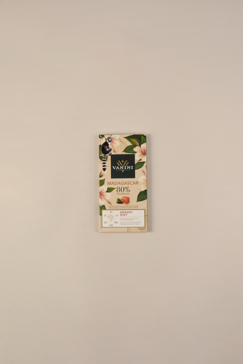 Video in cui la tavoletta di cioccolato fondente si scarta e si divide in pezzi. con affianco foglie di te chai e caramello. tutto su sfondo neutro beige.