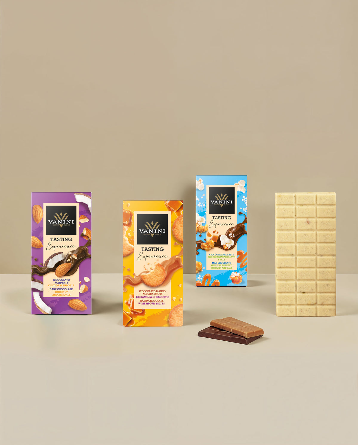 Selezione di tavolette Vanini Tasting Experience con esposizione di una tavoletta di cioccolato bianco aperta accanto alle confezioni della collezione. La composizione presenta gusti arricchiti da inclusioni selezionate come cocco, mandorle, granella di biscotto, popcorn caramellati, sale e pistacchio salato. Il design moderno e colorato delle confezioni è valorizzato da uno sfondo beige elegante che mette in risalto le diverse specialità di cioccolato.
